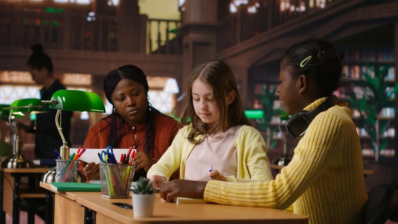 Mädchen im Vor-Teenageralter arbeiten in der Bibliothek gemeinsam mit ihrem Professor an Schulaufgaben.